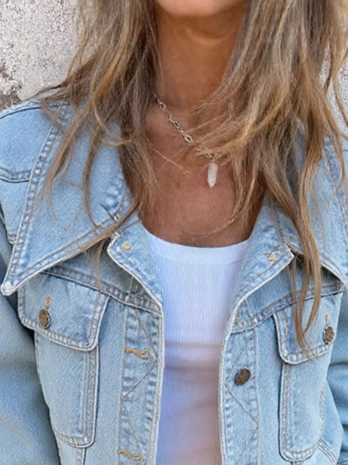 Close view of the light blue washed denim jacket collar, buttoned chest pockets and button front