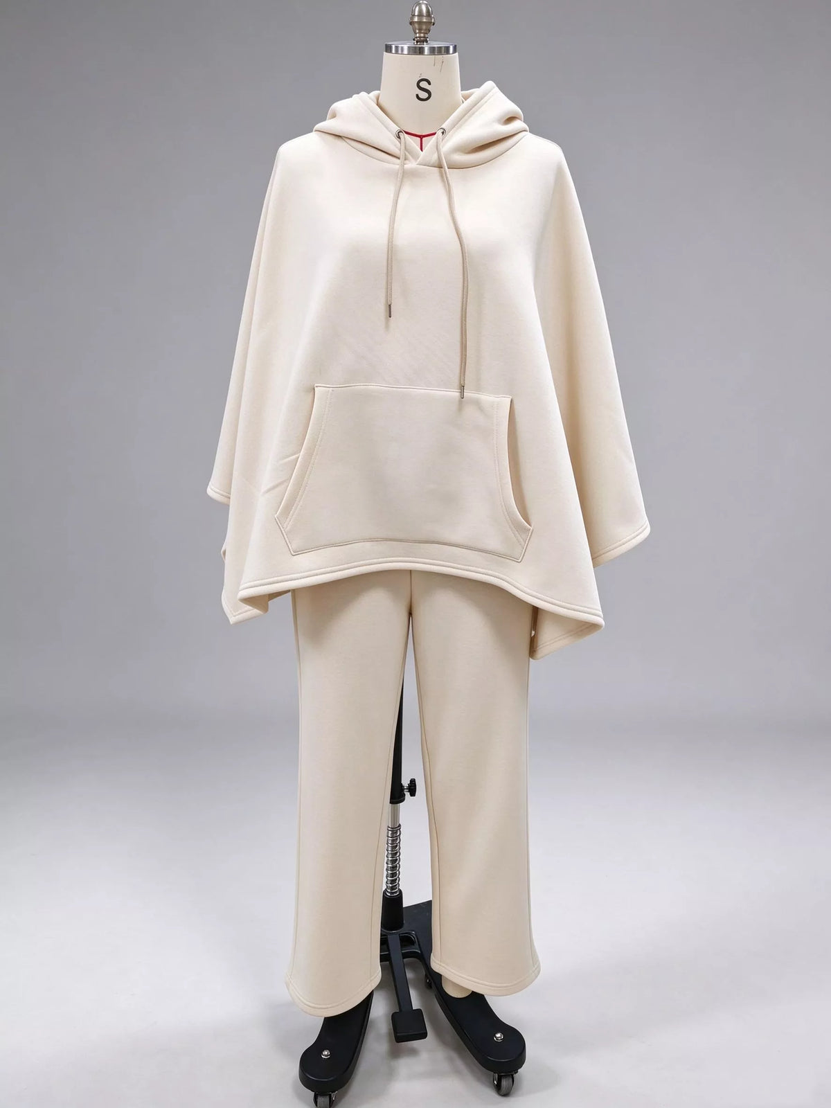 Beige hooded poncho top with a front pocket and drawstrings and matching wide-leg pants on a dress form, front view
