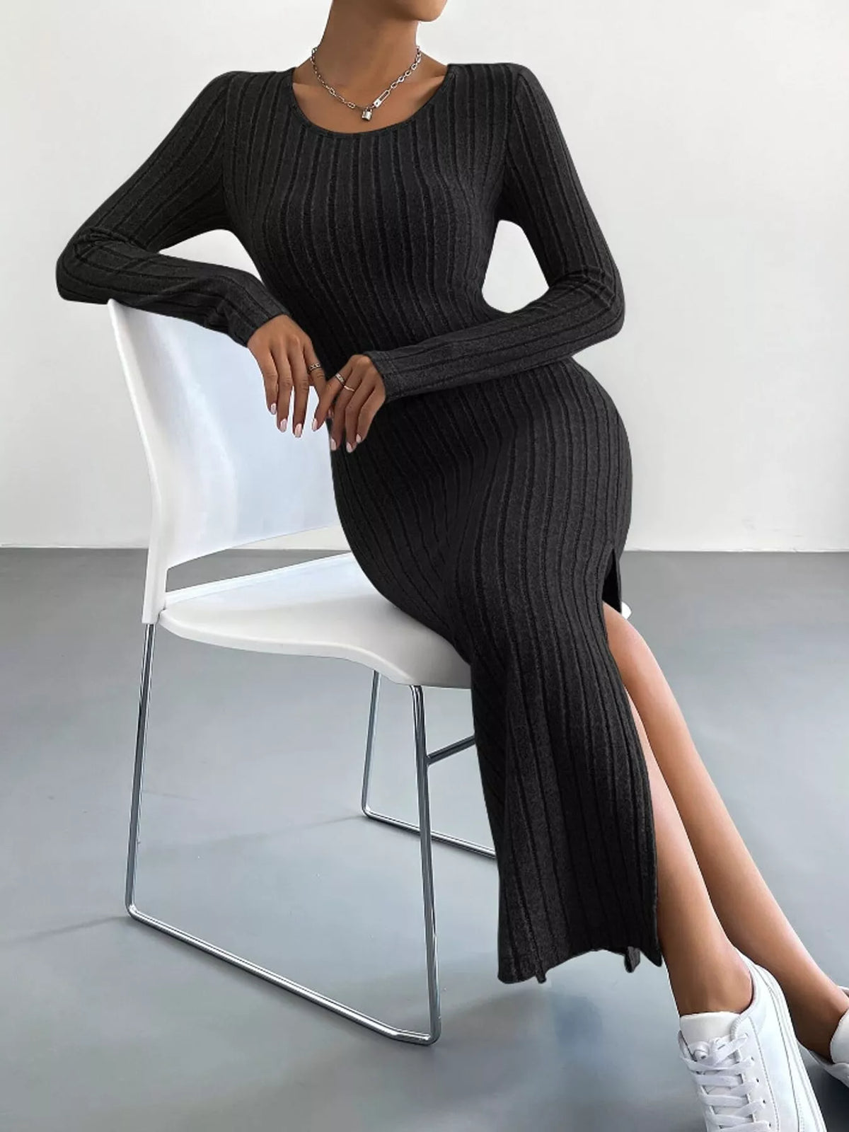 Black ribbed knit long-sleeve midi dress, seated view with the side slit visible
