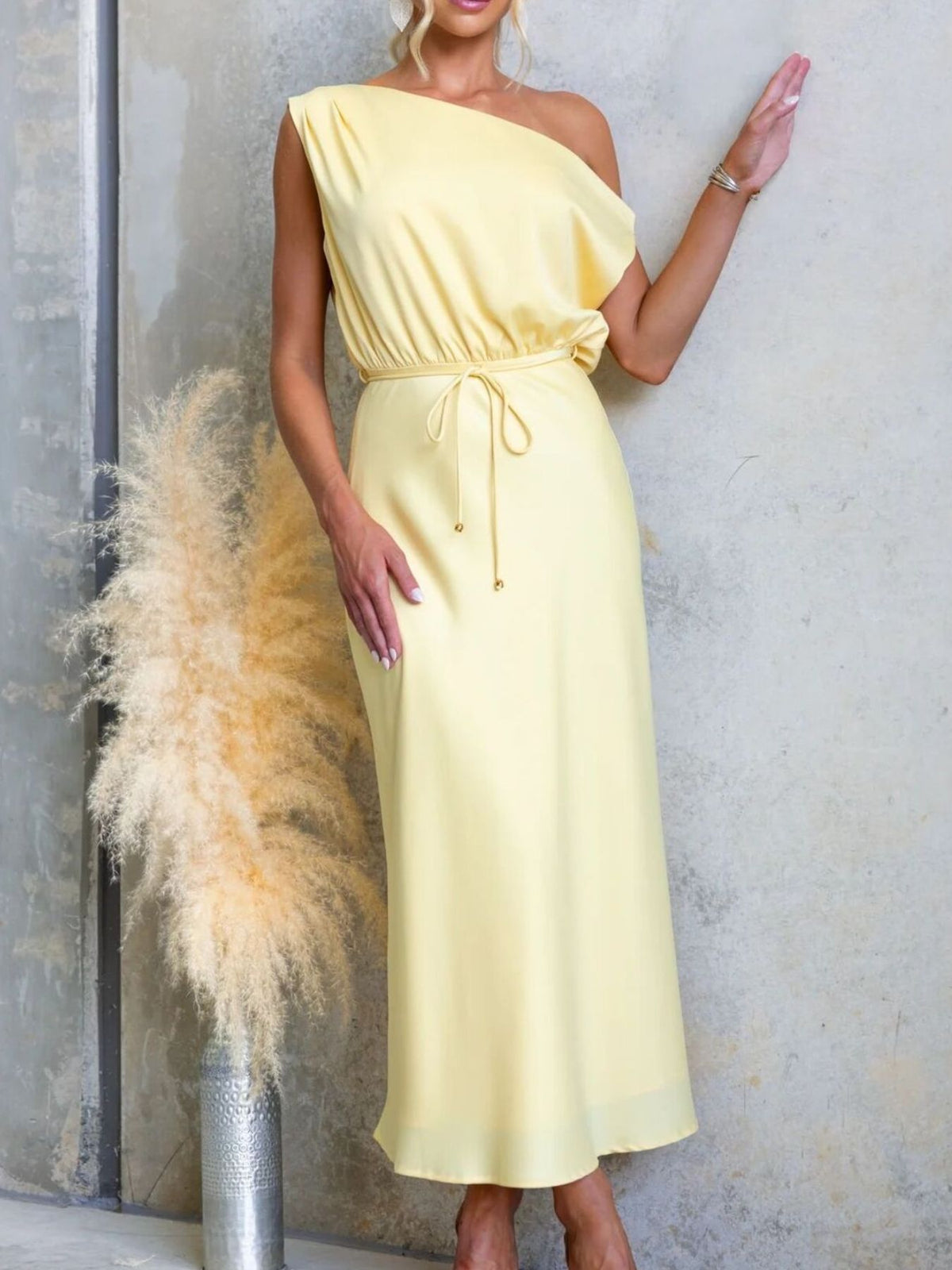 Yellow one-shoulder maxi dress with tie waist, front view with one hand raised