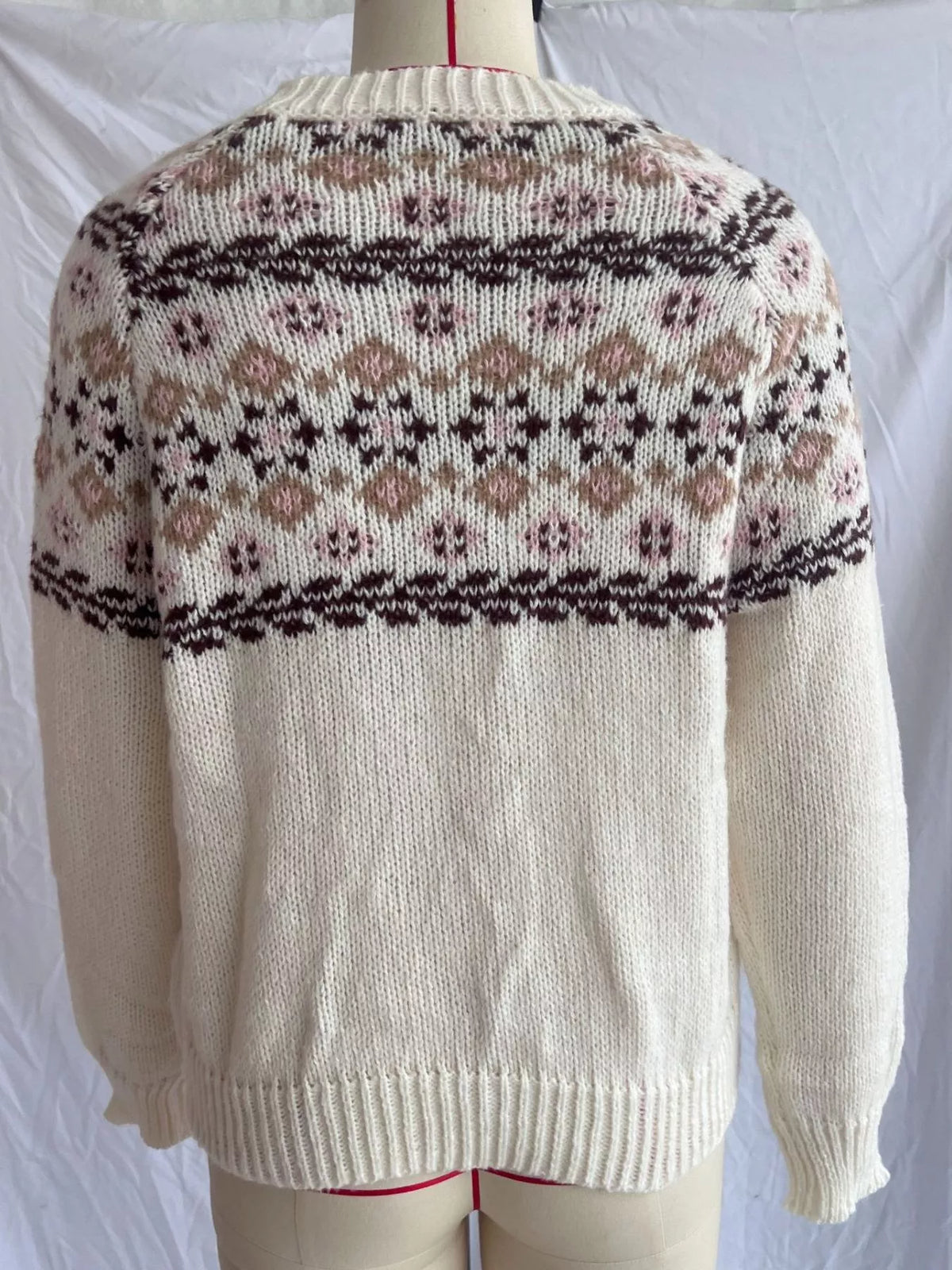 Back of the cream fair isle sweater on a dress form, showing the patterned yoke across the back and the ribbed hem