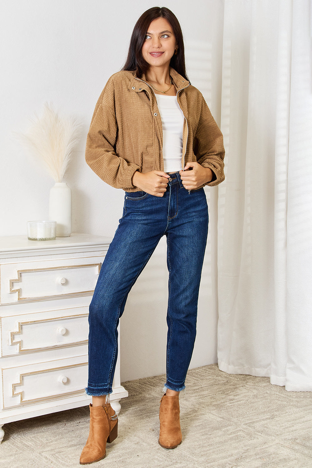 Full-length view of the camel cropped jacket worn open with a white top, blue jeans and ankle boots