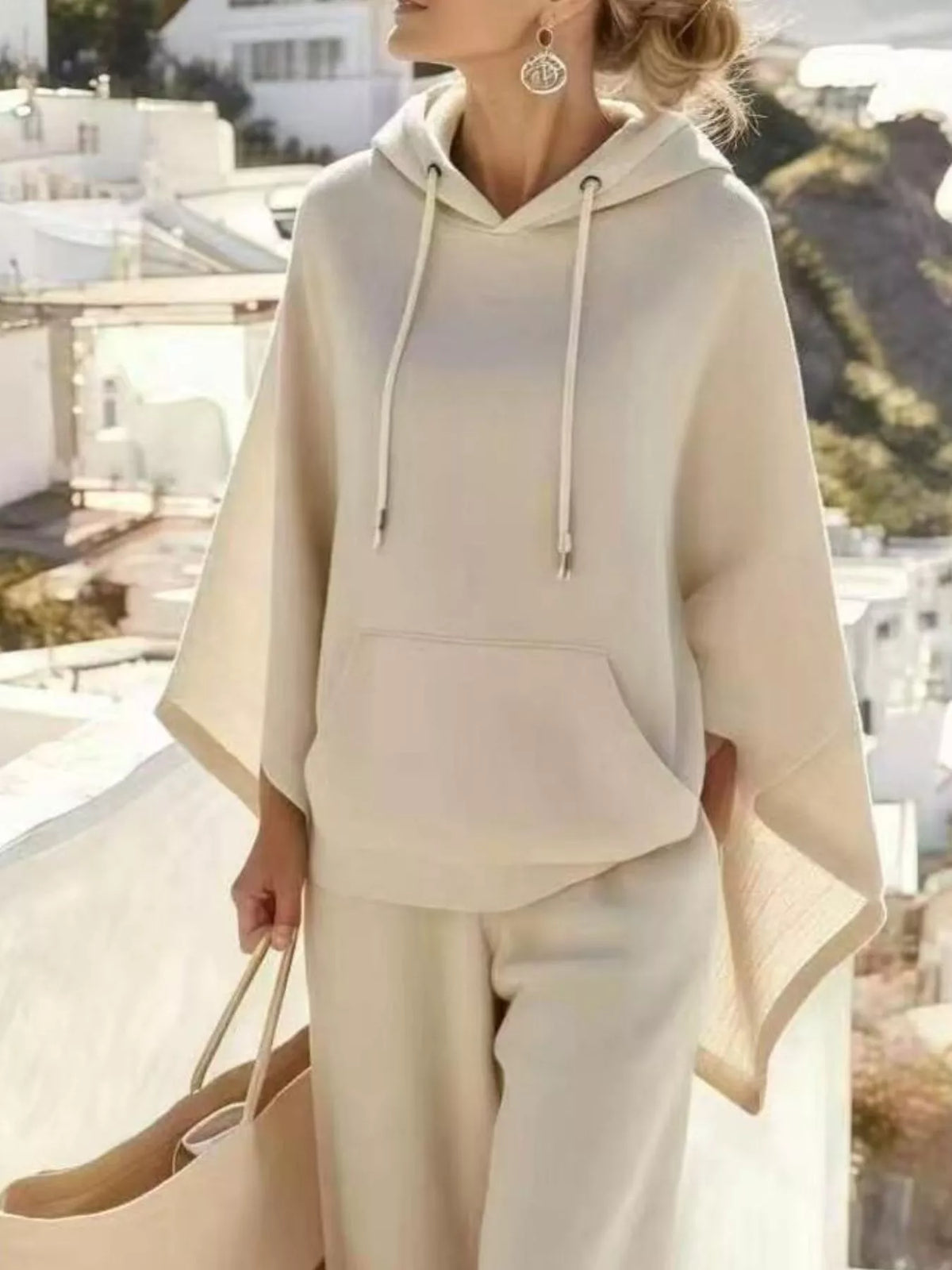 Close-up of the beige hooded poncho top showing the drawstrings, front pocket and draped side