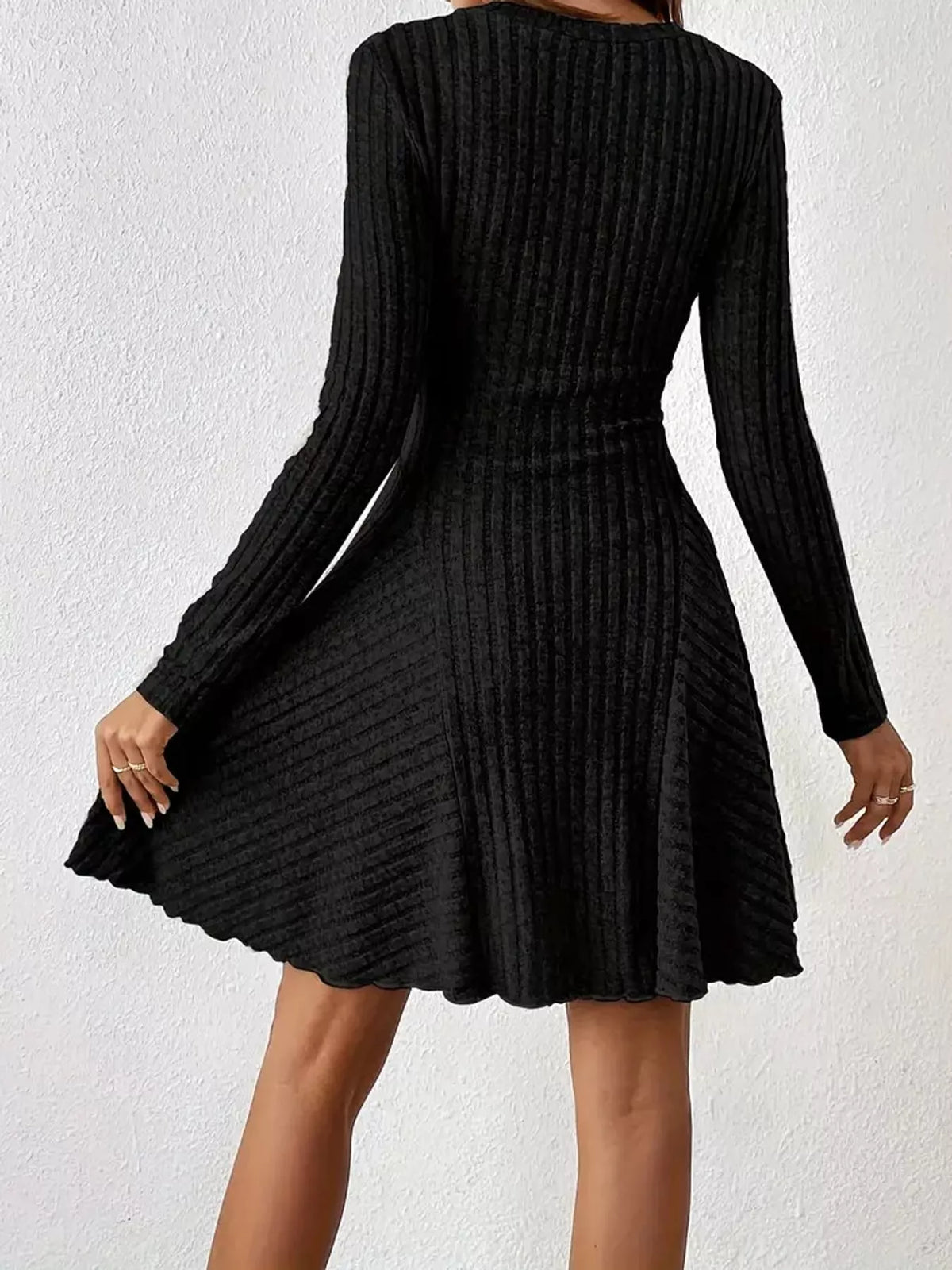 Back view of the Black ribbed knit long-sleeve flared dress with one hand on the skirt