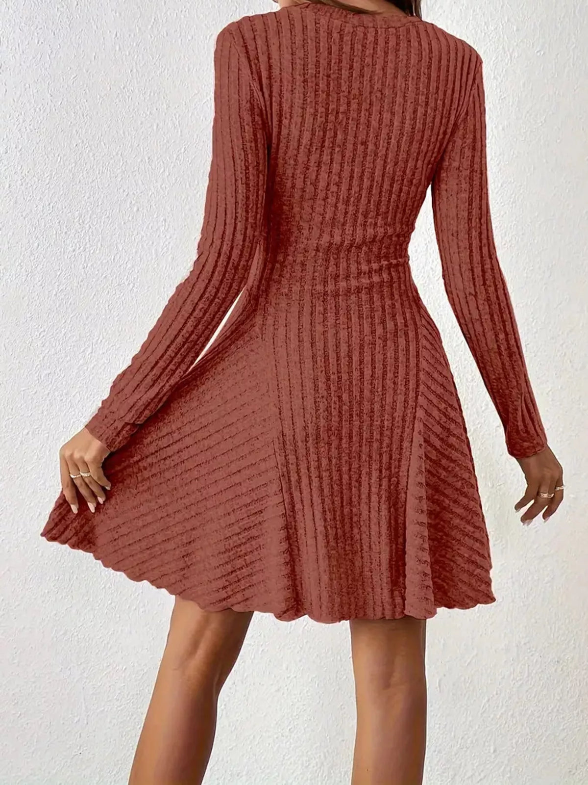 Back view of the Brick Red ribbed knit long-sleeve flared dress with one hand on the skirt