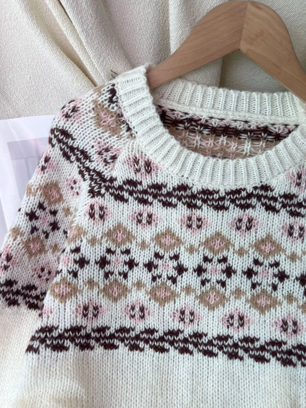 Close view of the ribbed round neckline and the yoke pattern in dark brown, taupe and soft pink on the cream sweater