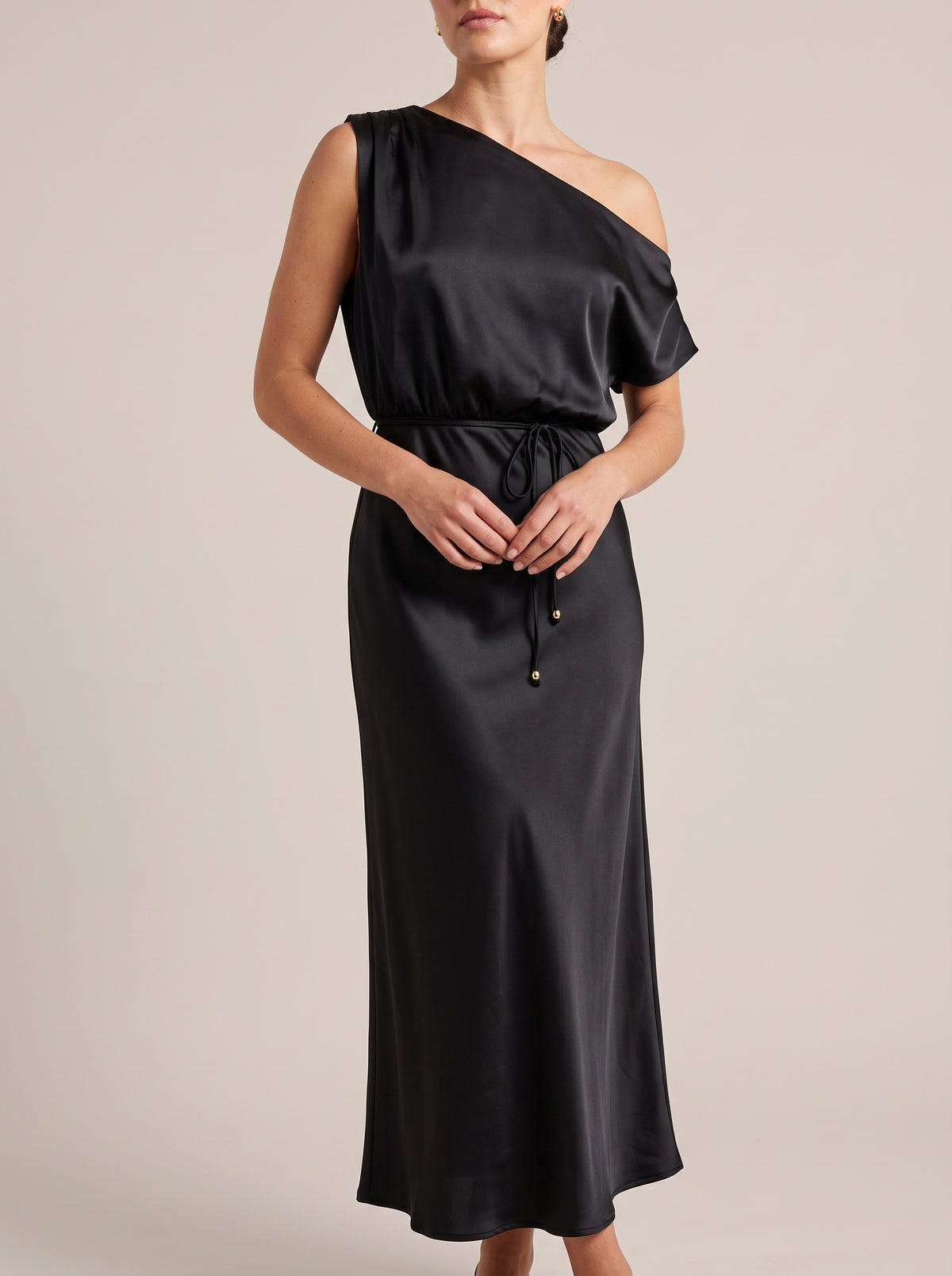 Black one-shoulder maxi dress with tie waist, front view with hands at the waist