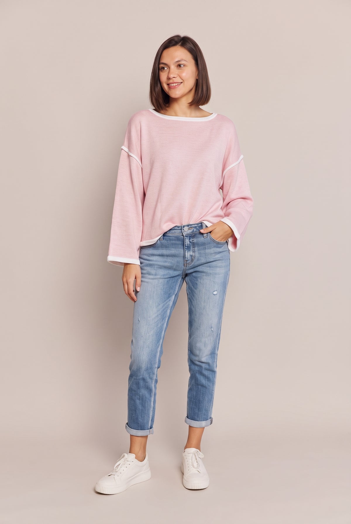 Full-length view of the blush pink knit top with white contrast trim, worn with cuffed blue jeans and white sneakers