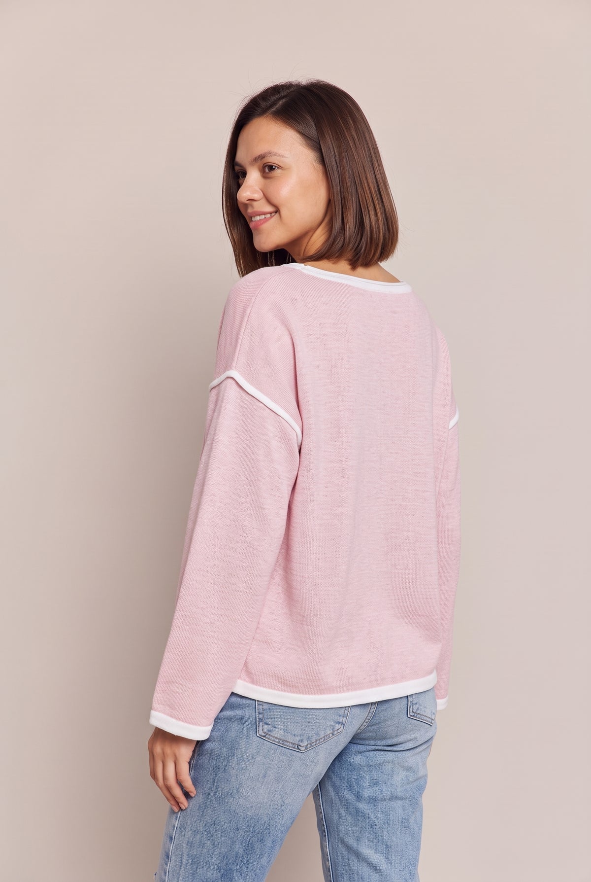 Back three-quarter view of the blush pink knit top showing the dropped shoulder seam with white trim and the white-edged hem