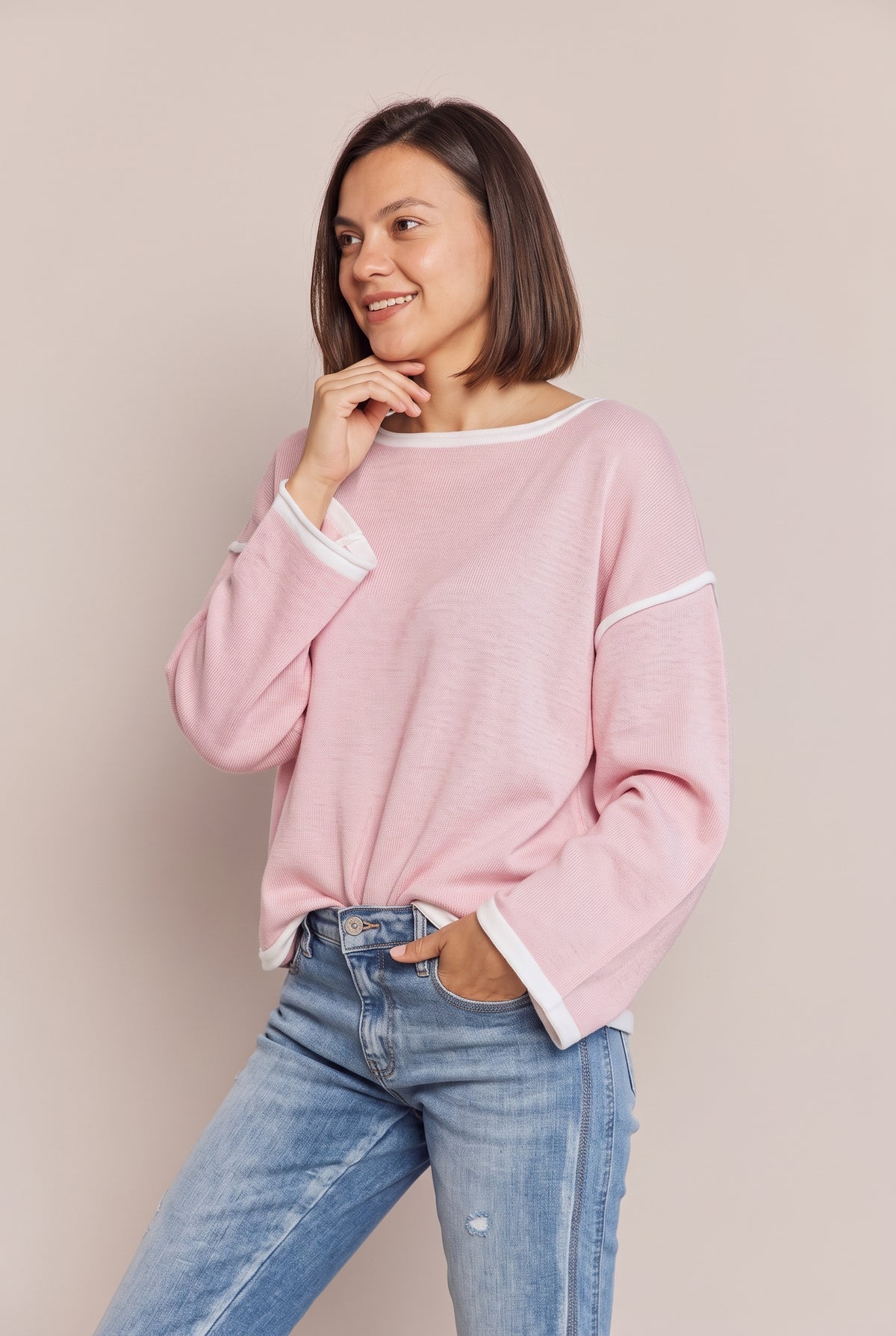 Three-quarter view of the blush pink knit top with dropped shoulders and open, white-edged cuffs, worn with blue jeans