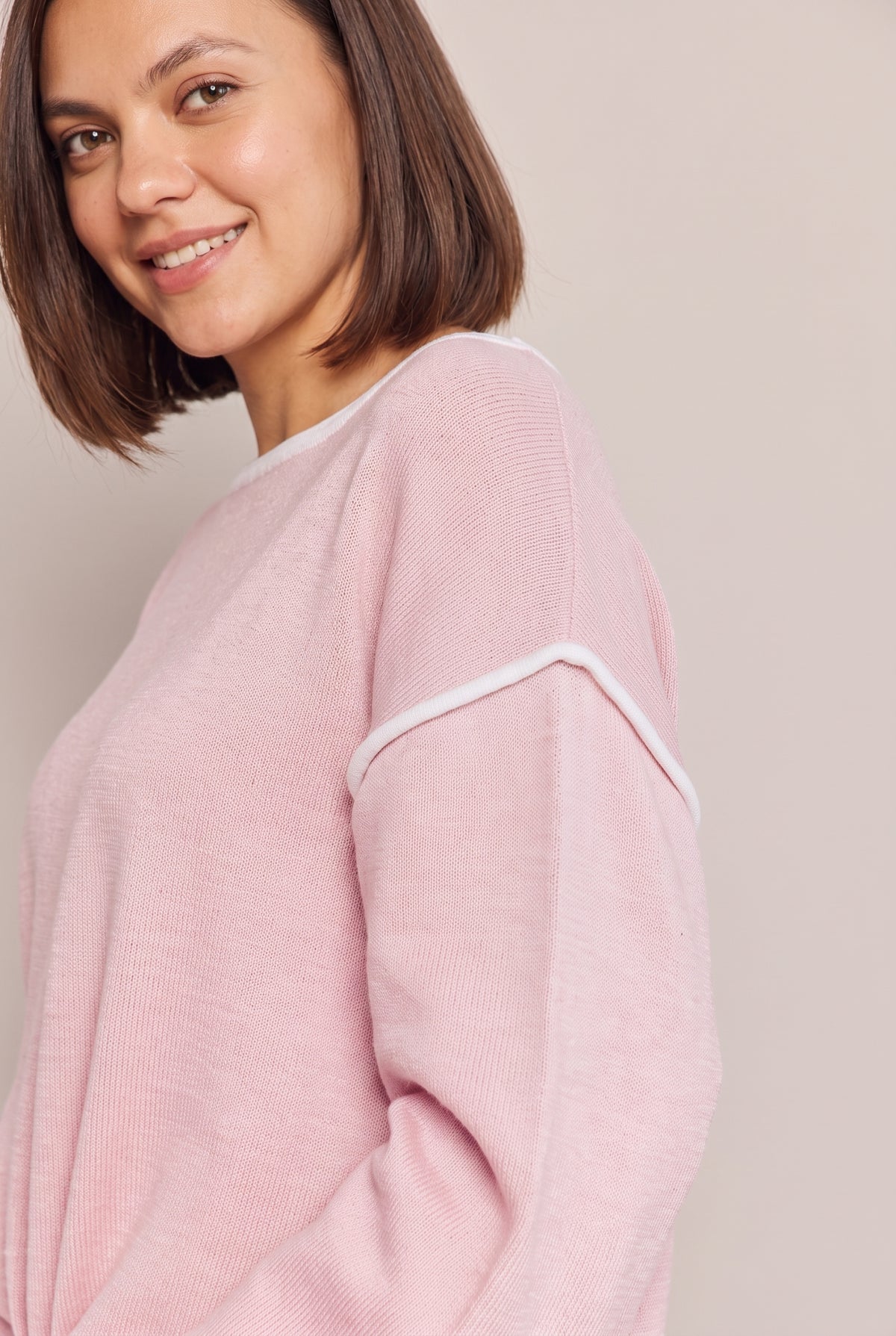Close-up of the dropped shoulder seam with white contrast trim on the blush pink knit top