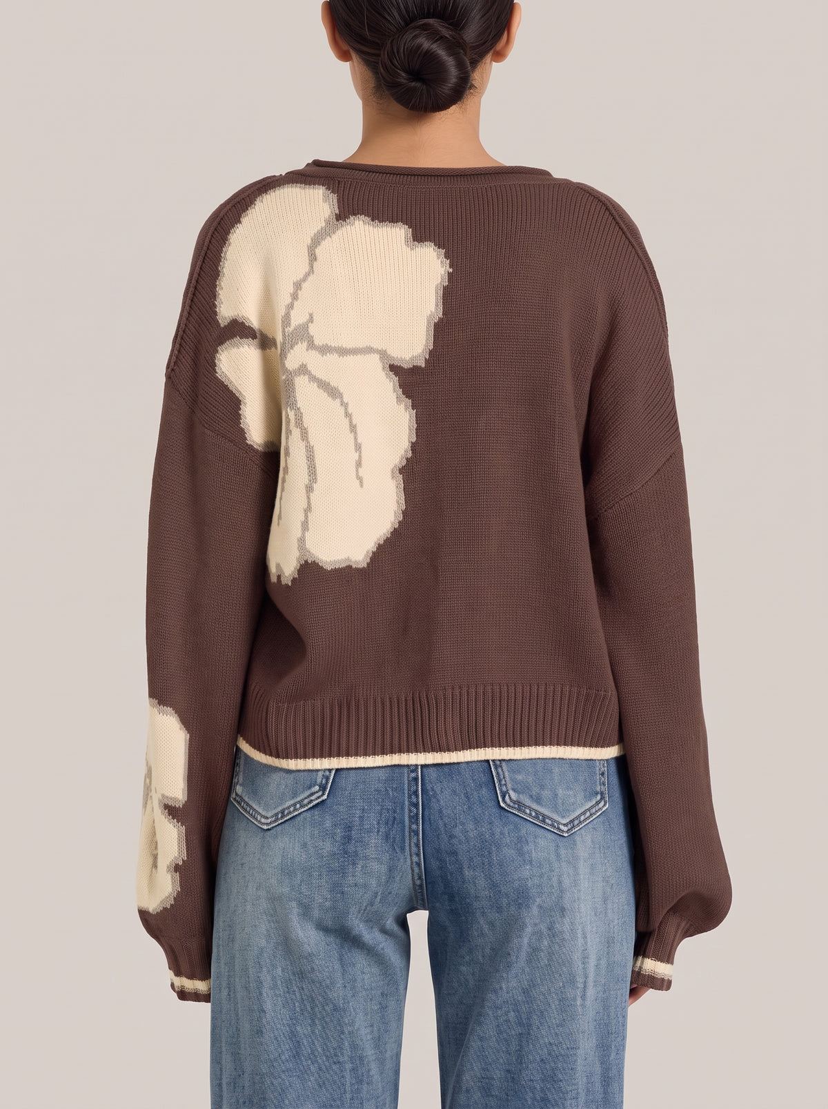 Back view of the brown floral knit cardigan with one large cream flower, a cream-tipped ribbed hem and striped cuffs