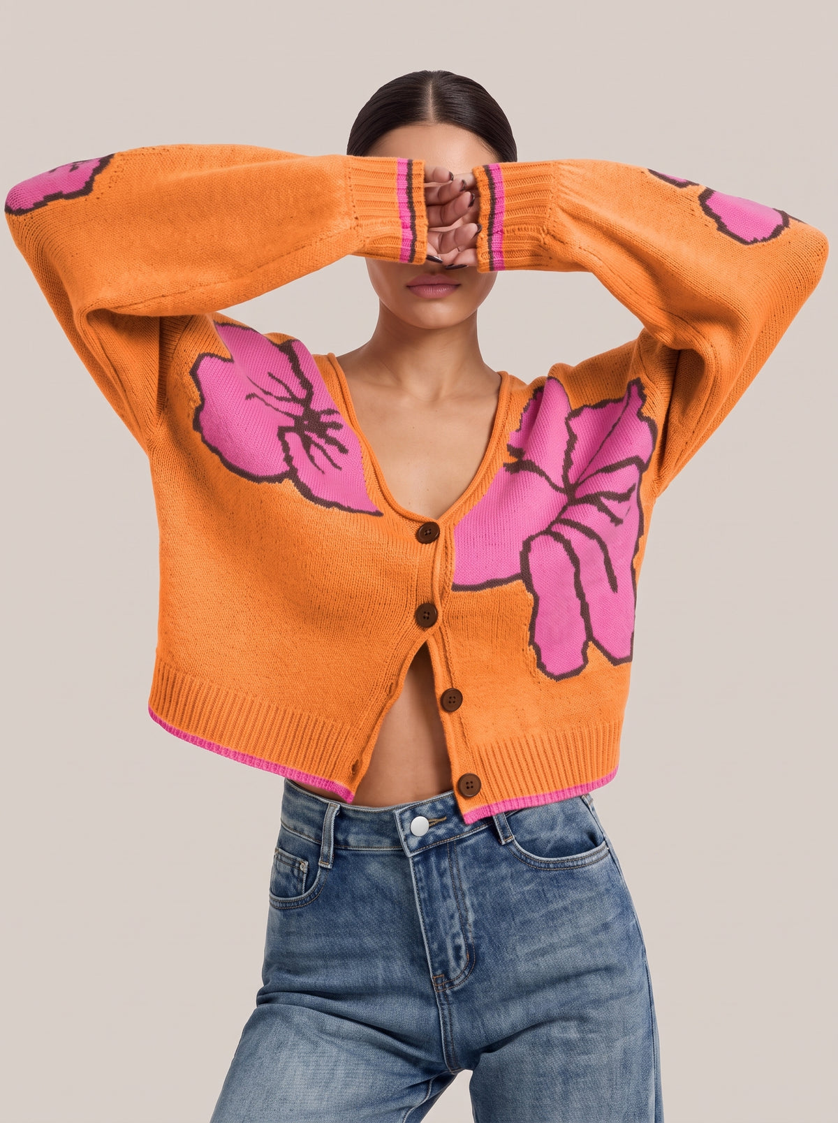 Orange floral knit cardigan with pink flowers, arms raised to show the pink-striped cuffs and pink-tipped hem