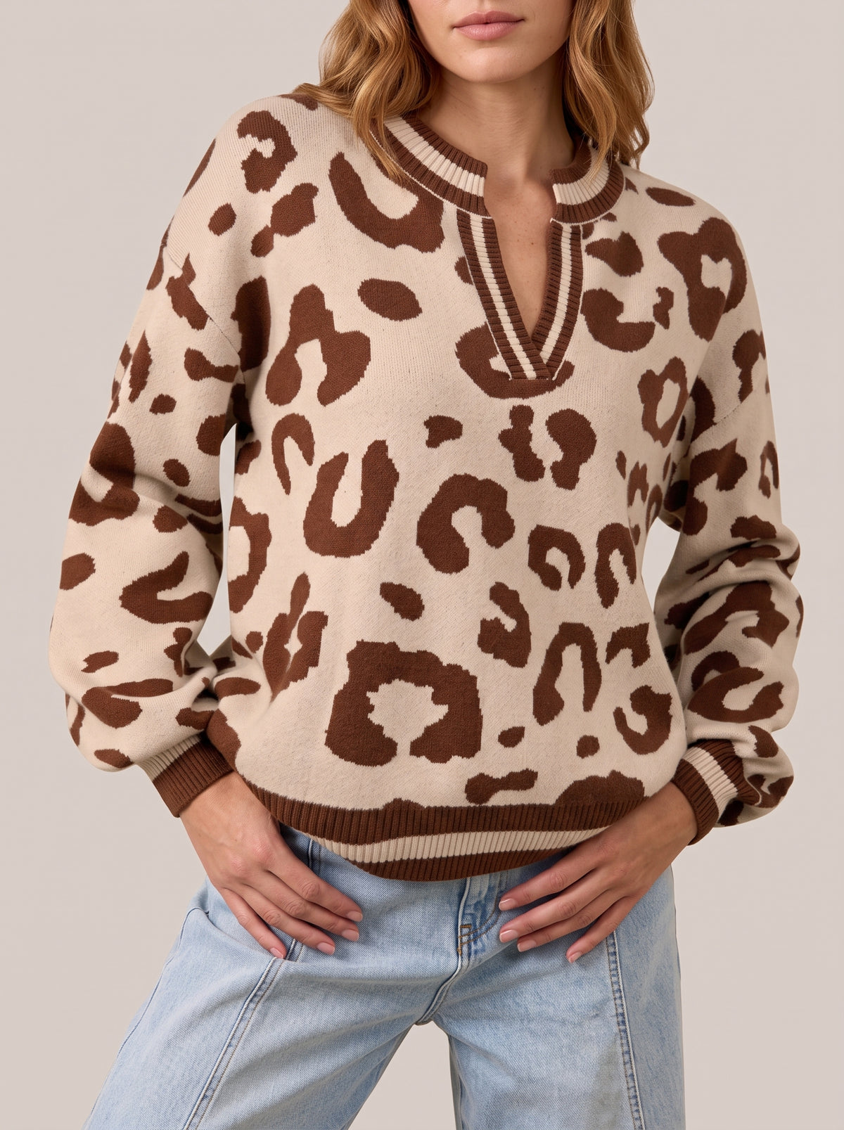 Leopard print knit sweater with brown spots on a light sand ground, a notched V neckline and brown and cream striped rib trim, front view
