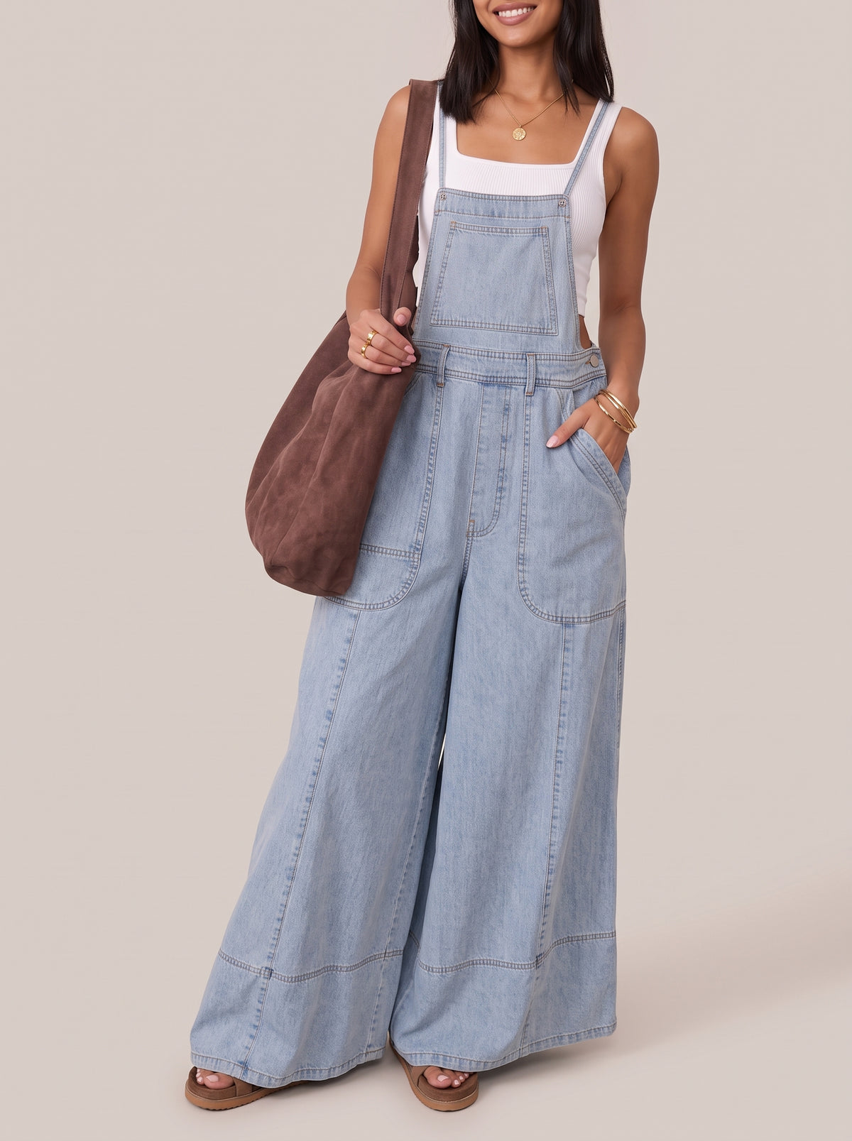 Light blue wide leg denim overalls, front view with hand in pocket and a brown shoulder bag