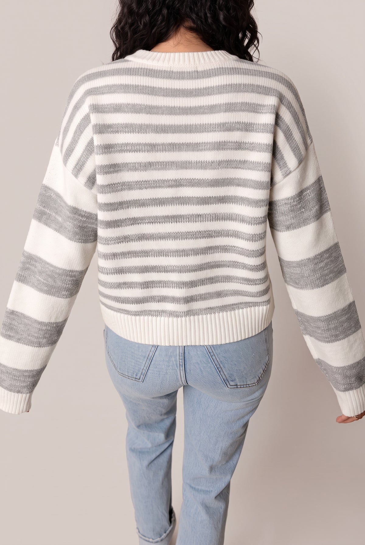 Back view of the grey and off-white striped sweater with dropped shoulders and a ribbed hem