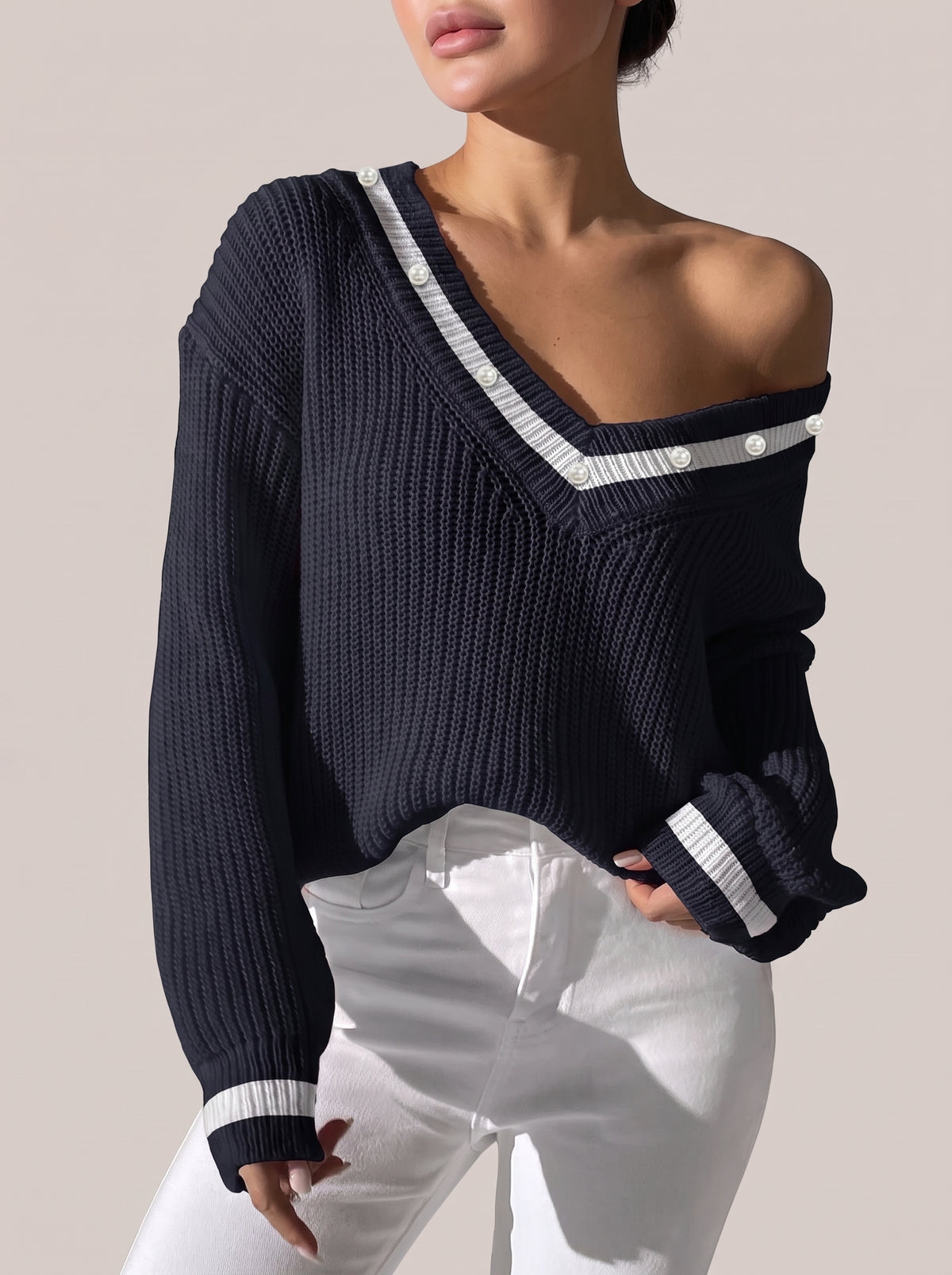 Dark navy V-neck sweater worn off one shoulder, with white trim and pearl-look beads along the neckline
